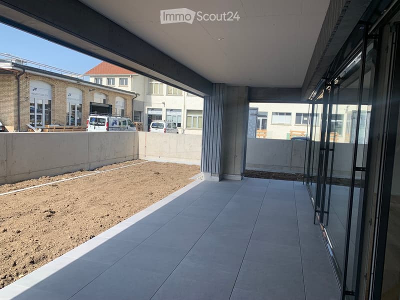 Balcony with tiled floor, glass railing, and view of a construction site with sand and parked vans.