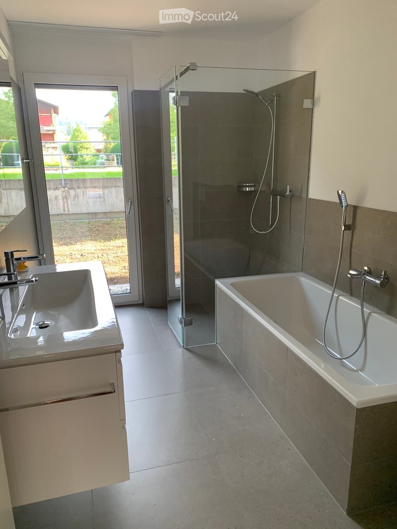 Modern bathroom with a large window, a bathtub, a sink, and a glass-enclosed shower area.