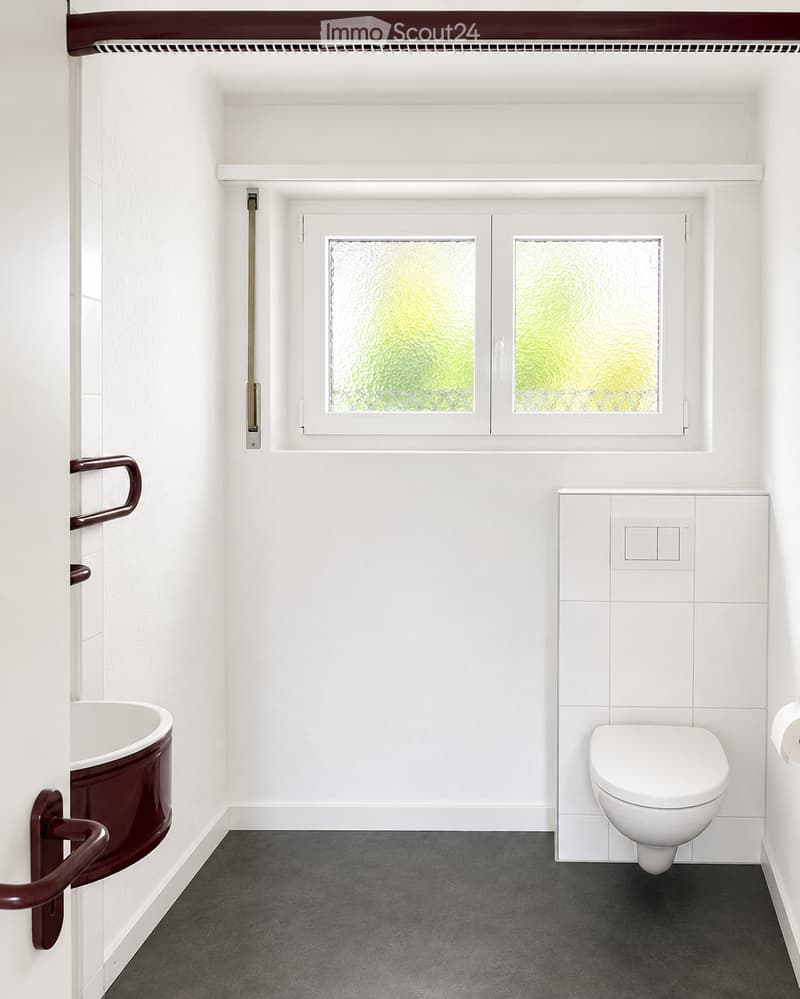 Modern bathroom with white tiled walls, a dark grey floor, a white toilet, a dark red sink, and a frosted glass window above.