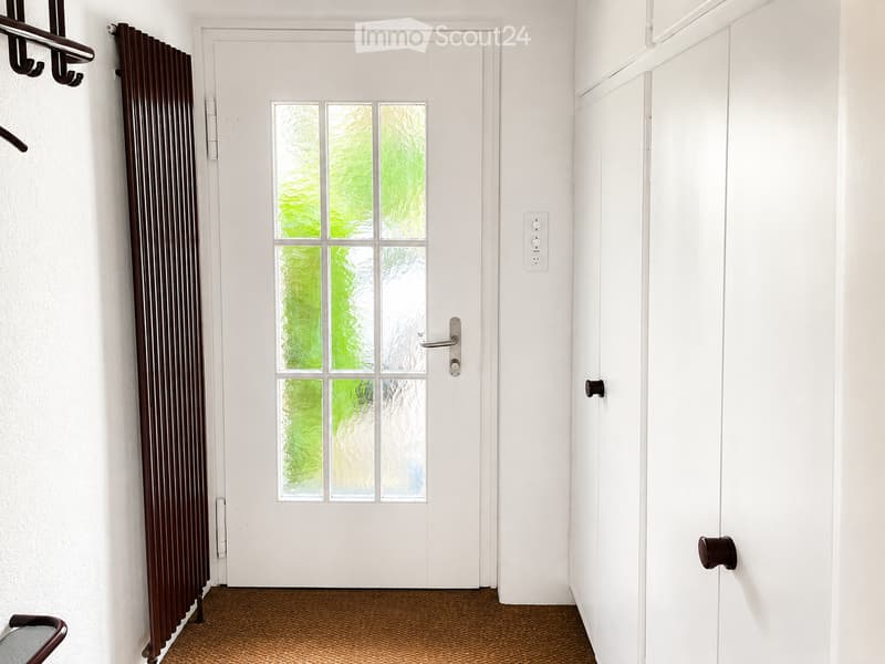 A clean, modern hallway with a white door featuring glass panels, a brown radiator, and a patterned brown carpet floor.