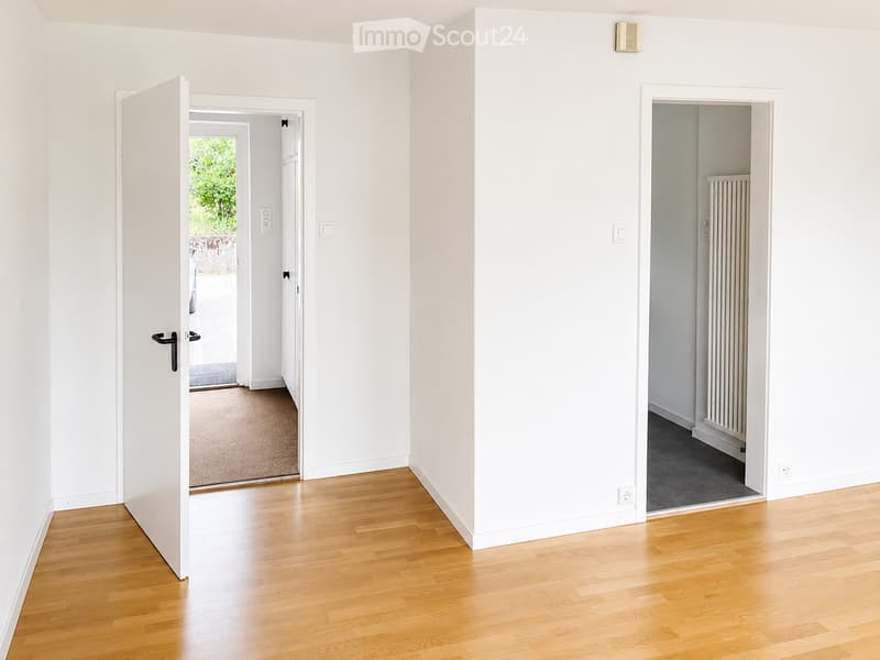 Empty hallway with light wooden flooring, white walls, and two open doors leading to adjacent rooms.