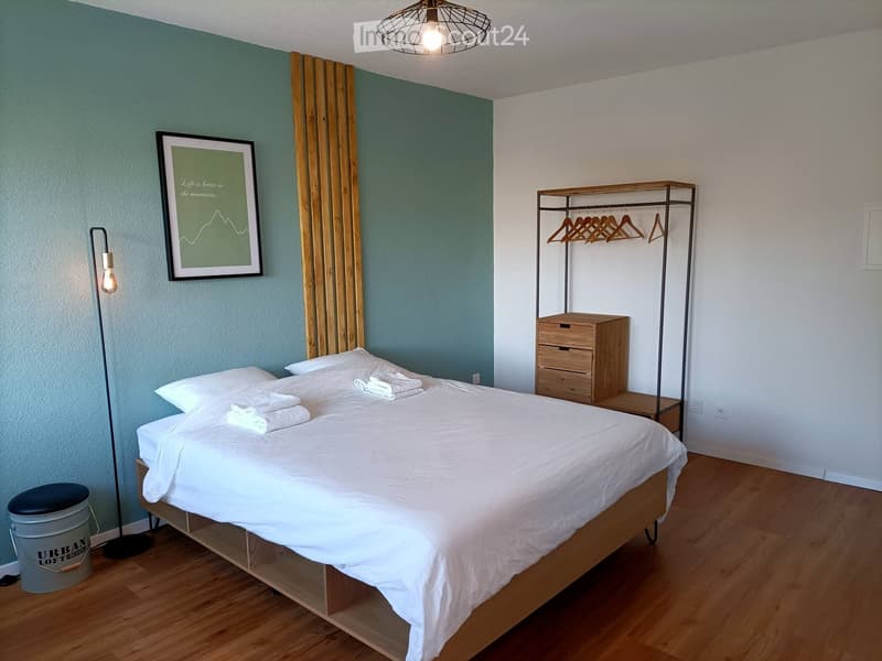 Cozy bedroom with a white bed, wooden nightstand, floor lamp, picture frame, wooden shelf, and hanger rack.