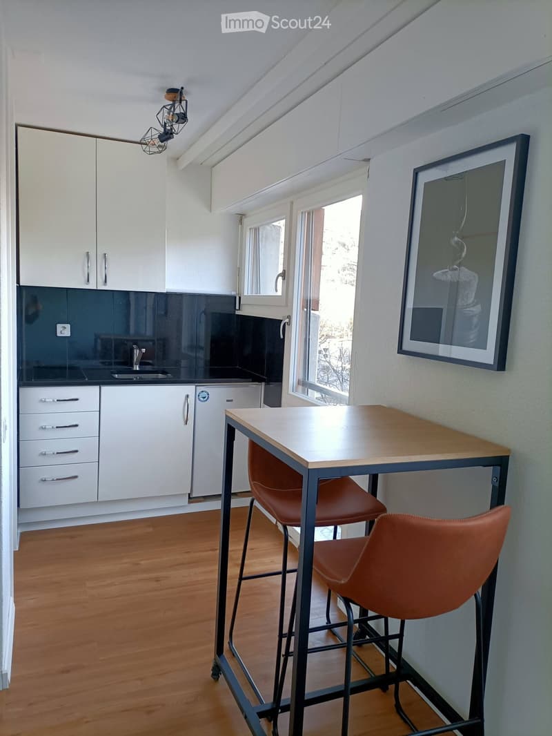 Modern kitchen with white cabinets, dark backsplash, wooden floor, and a small dining area with a table and stools.