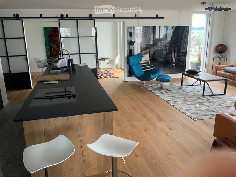 open kitchen with central island, wood flooring, sliding door, black bar counter, blue chair, glass coffee table, white stools, beige area rug