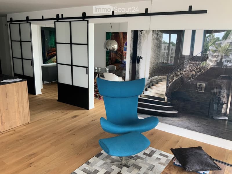 open space with wooden floor, large windows, white walls, glass doors, blue armchair, ottoman, rug, picture on wall
