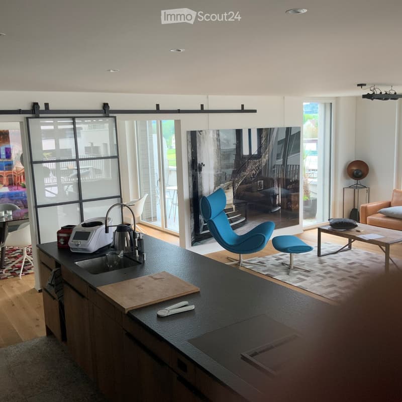 Modern kitchen with wooden countertops, island, open plan with living room, large windows, sliding doors to a balcony, carpet flooring.
