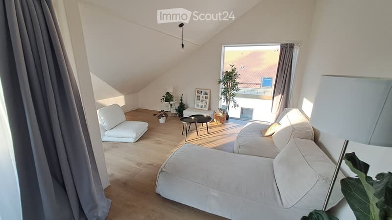 Bright living room with wooden flooring, white sofa, chair, small tables, and decorative plants.