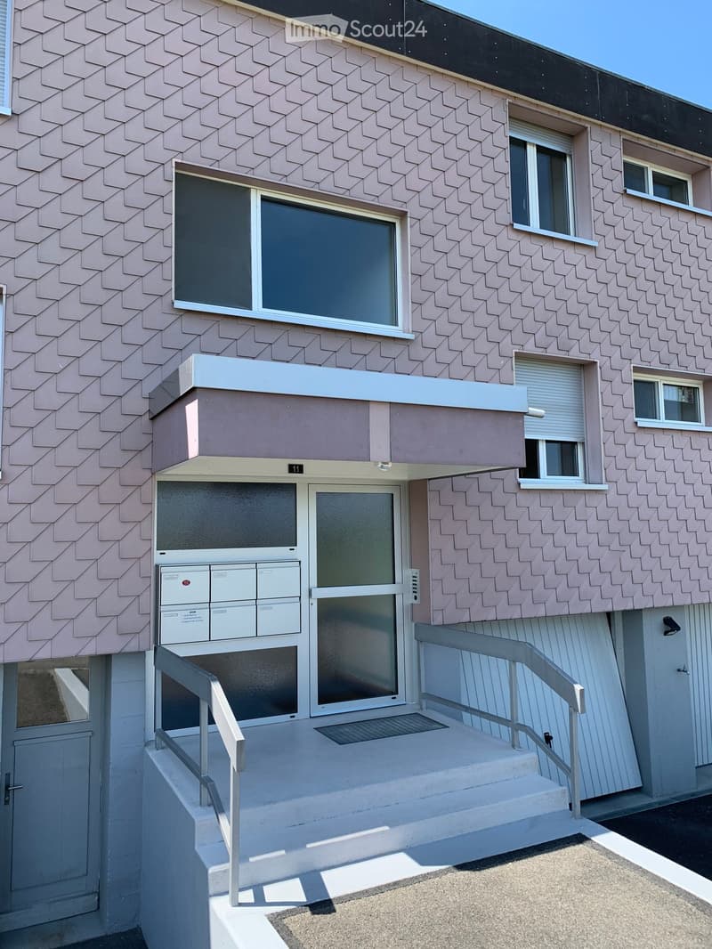 Modern multi-story building with pink patterned facade, white-framed windows, and a raised ground floor entrance with stairs and railings.