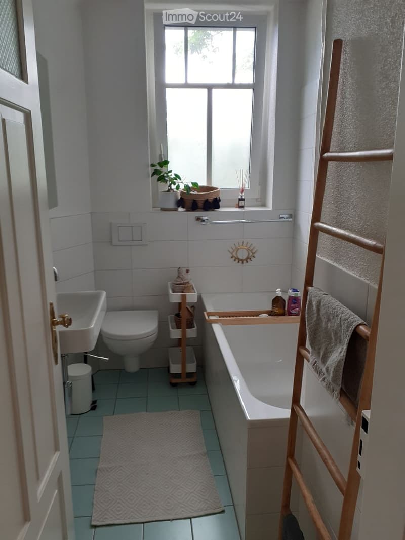 Bathroom with a bathtub, toilet, sink, towel, plant, and decorative tray on the windowsill.