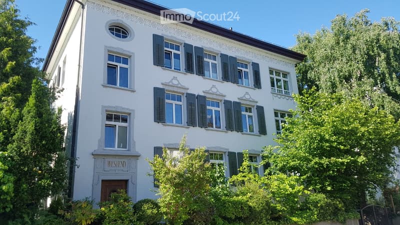 A two-story white house with decorative trim, multiple windows with shutters, and a well-maintained garden.