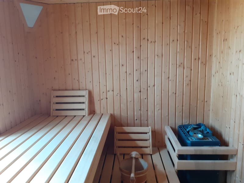 Wooden sauna interior with benches, a wooden bucket, and a small wooden crate holding items.