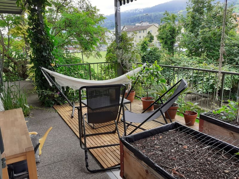 Balcony with wooden decking, lounge chairs, hammock, potted plants, and a raised garden bed.