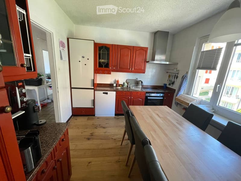 Bright kitchen with wooden flooring, red cabinets, white appliances, and a dining area with a wooden table and chairs.