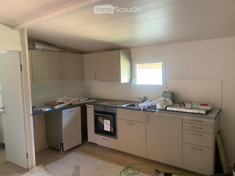 Kitchen with light-colored cabinets, stainless steel appliances, and a window above the sink. The space is partially furnished with construction materials and tools.