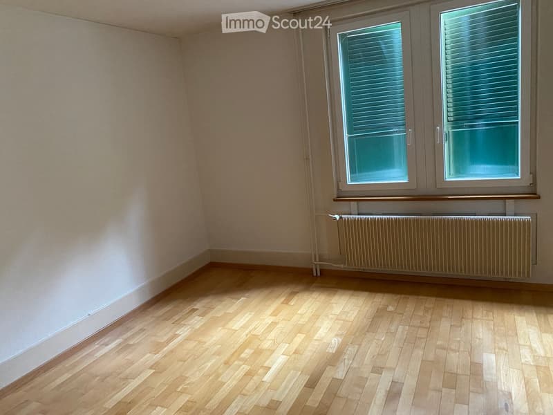 Empty room with wooden flooring, light-colored walls, and a radiator below a window with blinds.
