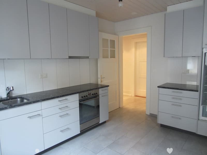 Modern kitchen with white cabinets, black granite countertops, stainless steel sink and oven, and a doorway leading to another room.