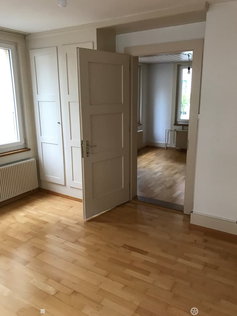 Empty hallway with wooden flooring, white walls, and a partially open door leading to another room.