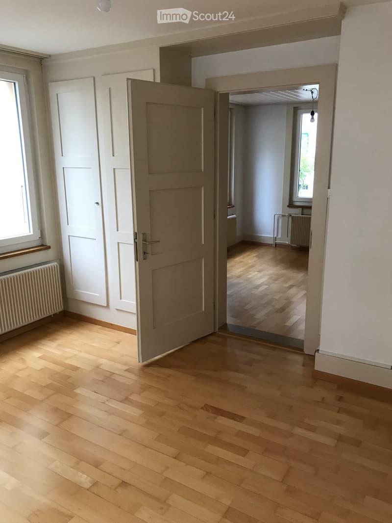 Empty hallway with wooden flooring, white walls, and a partially open door leading to another room.