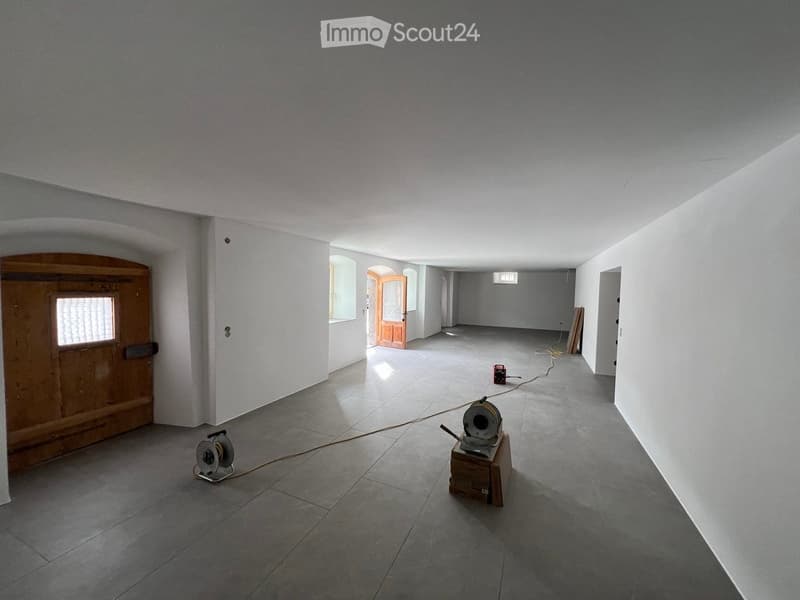 Empty room with grey tiled floor, white walls, and several doors leading to other spaces. Some construction tools and equipment are visible.