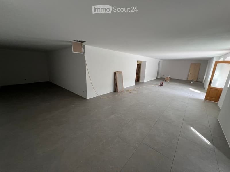 Empty room with grey tiled floor and white walls, featuring a wooden door and a small opening in the ceiling.