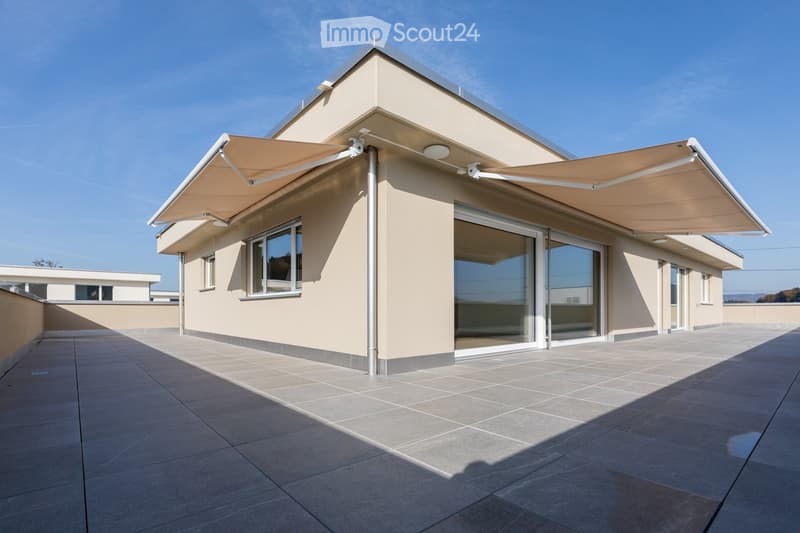Modern building with a tiled roof, beige exterior walls, large windows, and retractable awnings over the entrance.