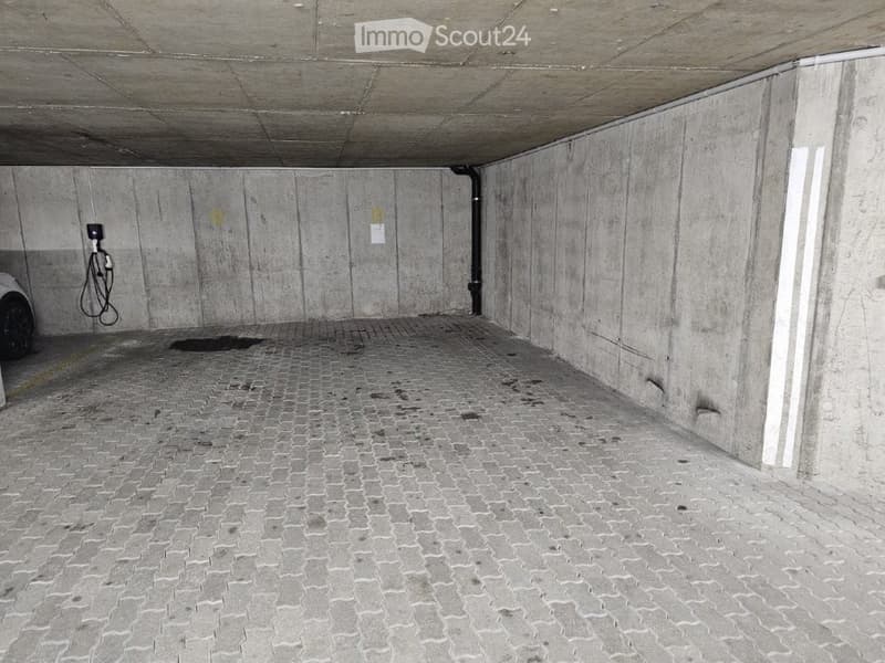 Underground parking space with concrete walls and ceiling, tiled floor, and a charging station for electric vehicles.