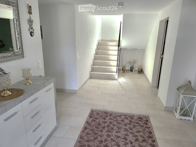 Entrance hall with white tiles, white cabinet, mirror, rug, staircase, and decorative items
