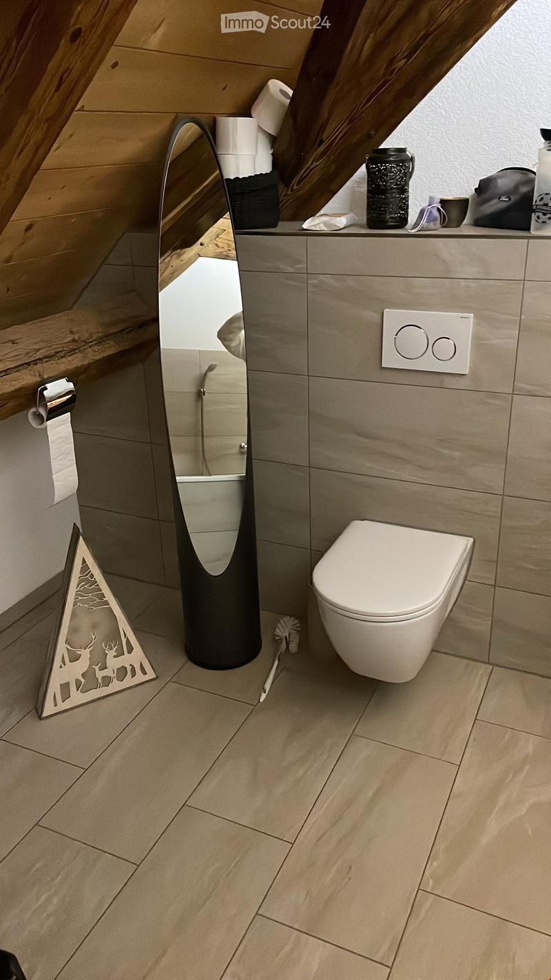Modern bathroom with beige tiles, a toilet, a large mirror, and decorative wall piece featuring deer silhouettes.