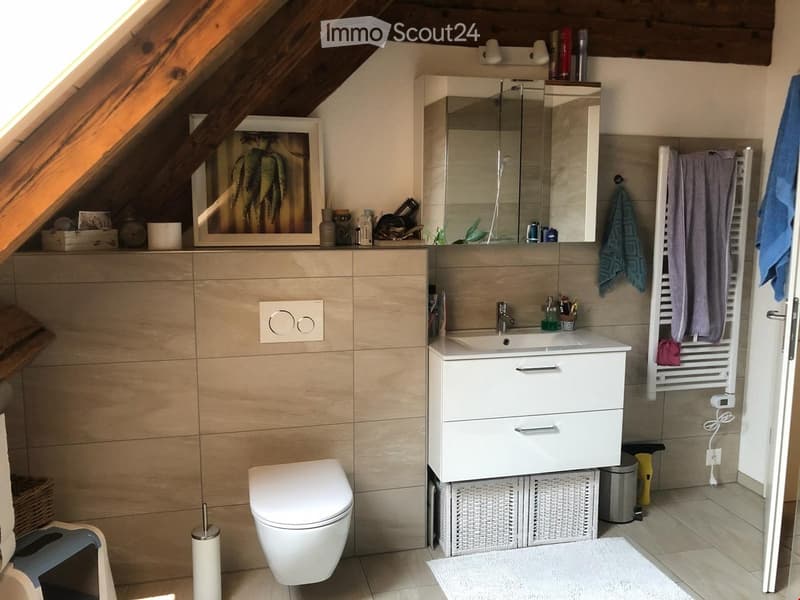 Modern bathroom with a white sink, mirror, toilet, and towel rack. Features a framed picture on the wall and a wicker basket under the sink.