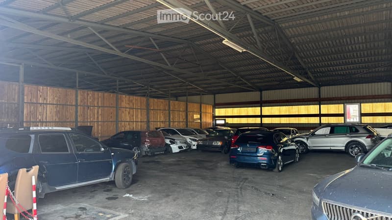 Large indoor garage with multiple parked cars, including SUVs and sedans, under a metal roof with wooden panel walls.