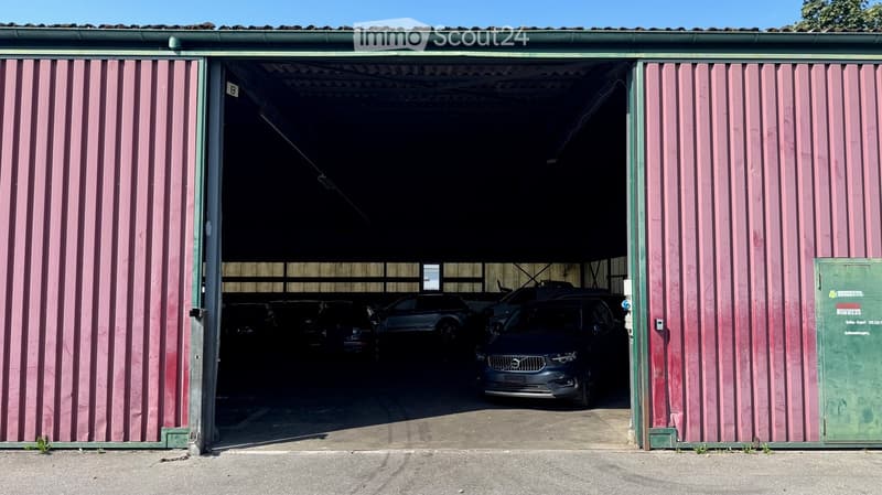 Open garage with several parked cars inside, pink vertical siding, green trim, and a sign on the right side.