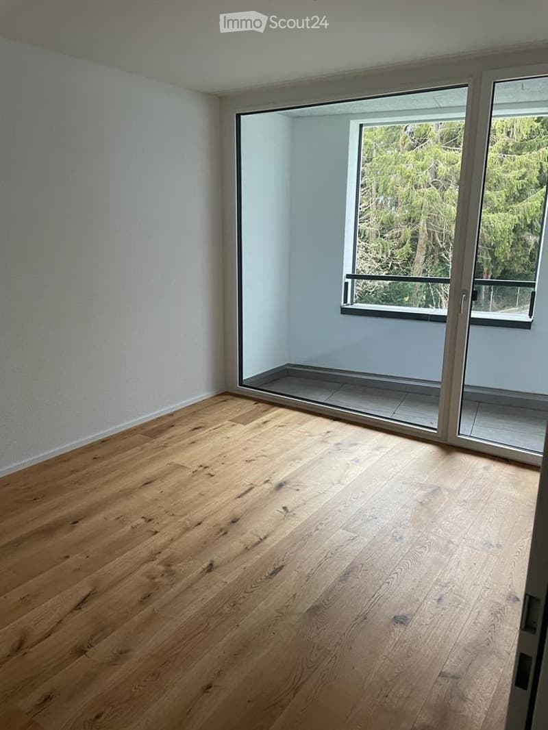 Empty room with light wooden flooring and large glass sliding doors leading to a balcony area.