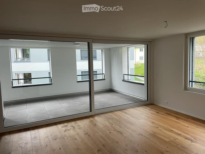 Empty room with wooden flooring, large sliding glass doors leading to a balcony area, and large windows providing natural light.
