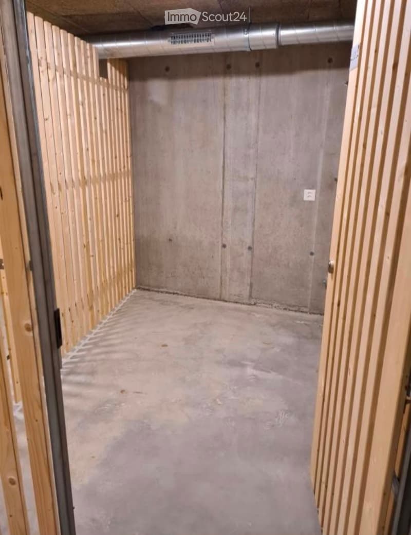 Empty room with unfinished concrete walls and floor, wooden framing on the sides, and exposed ductwork on the ceiling.