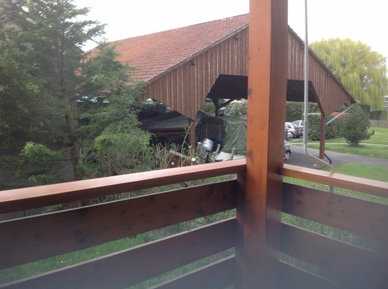 Wooden balcony overlooking a wooden shed, covered area, and surrounding greenery.