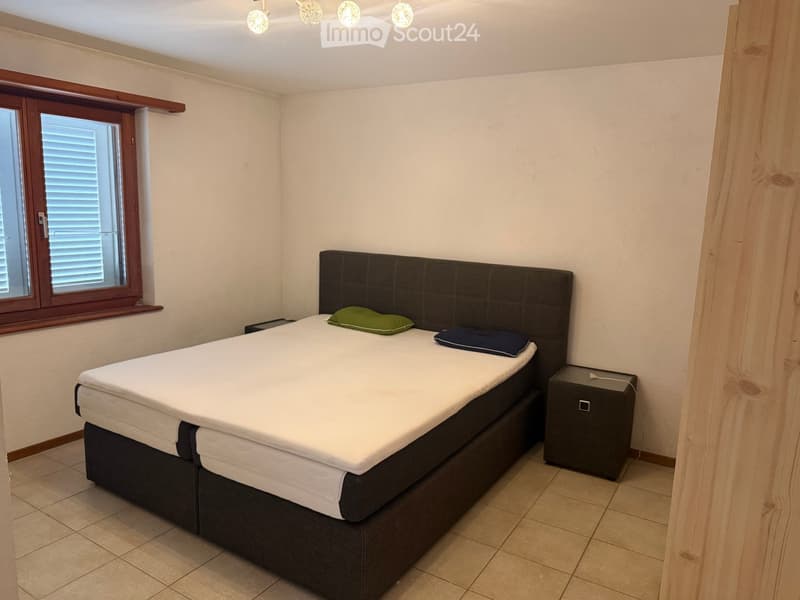 Bedroom with a double bed, nightstand, and pillows, featuring a large window with blinds and tiled flooring.