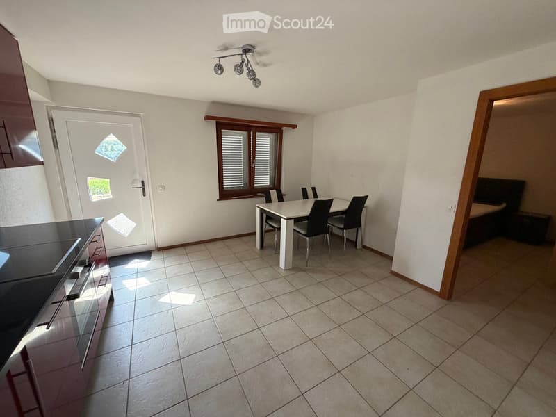 Open-plan kitchen and dining area with tiled flooring, white dining table, four chairs, and dark kitchen cabinetry.