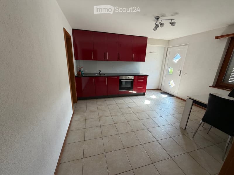 Modern kitchen with red cabinets, a sink, an oven, and a dining area with a table and chair.