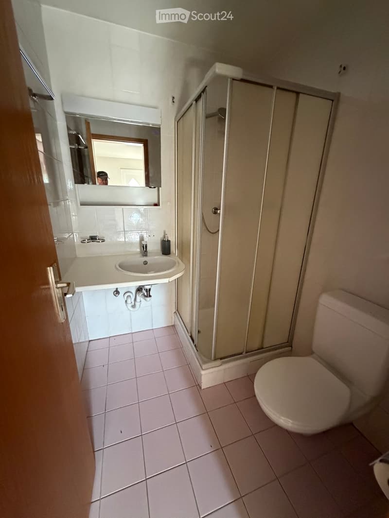 Small bathroom with white tiles, a sink, a toilet, a shower, and a mirror above the sink.
