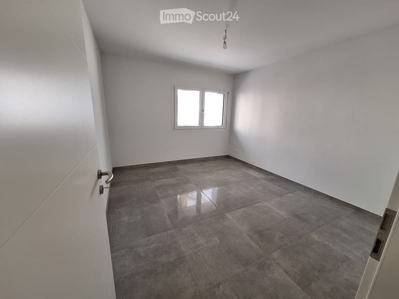 Empty room with grey tiled floor, white walls, and a window with two panes. No furniture or equipment present.