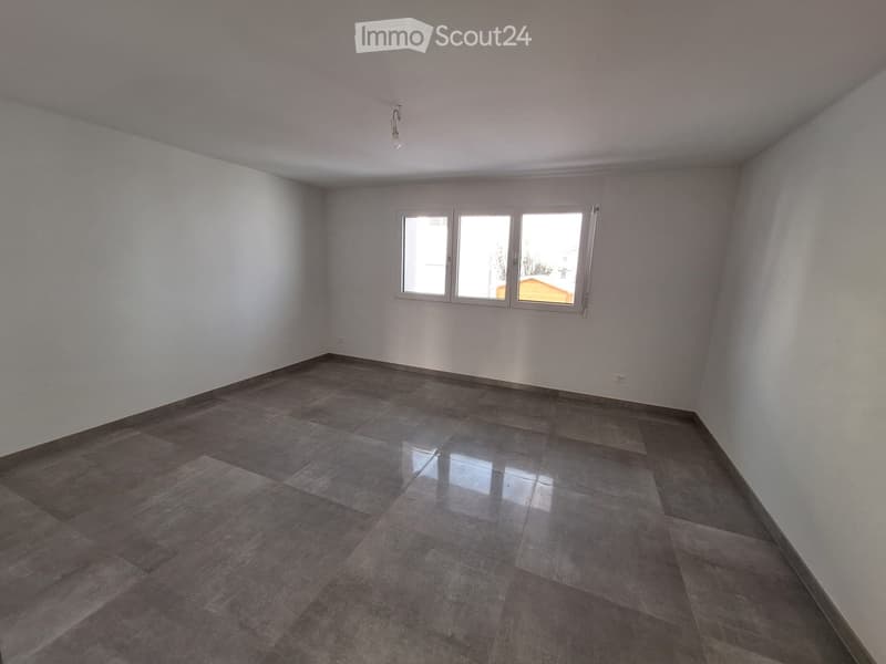 Empty room with light grey tiled floor and white walls, featuring a single window with three panes and a single light fixture on the ceiling.