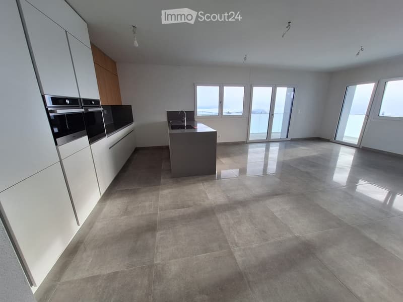 Modern kitchen with white cabinets, stainless steel oven, central island with sink and faucet, large windows and sliding doors leading to a balcony.