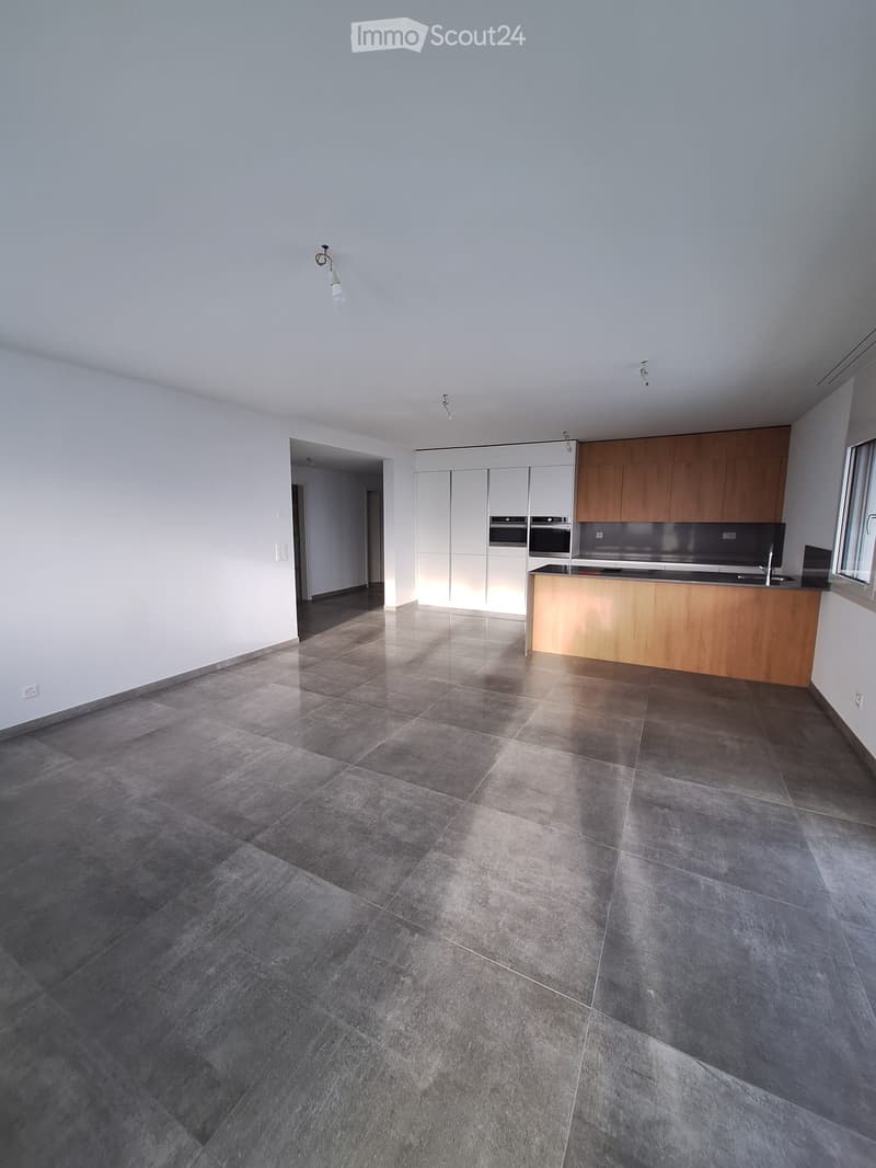 Empty kitchen with grey tiled floor, white cabinets, and a wooden countertop. No appliances or furniture are present.