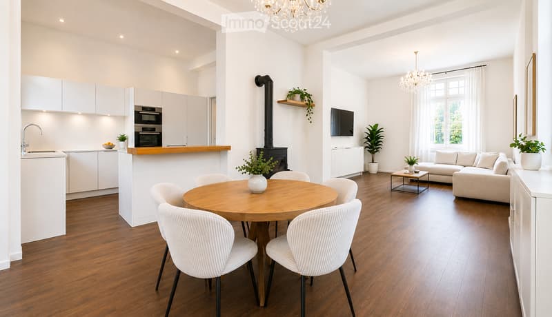 Open-plan living and dining area with a modern kitchen, white cabinets, a round wooden dining table with six chairs, a cream-colored sofa, a coffee table, a fireplace, and a chandelier.