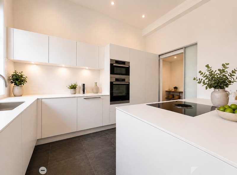 Modern kitchen with white cabinets, stainless steel appliances, and a central island with an induction cooktop. Includes a sink, faucet, decorative vases, and a bowl of fruit on the counter.
