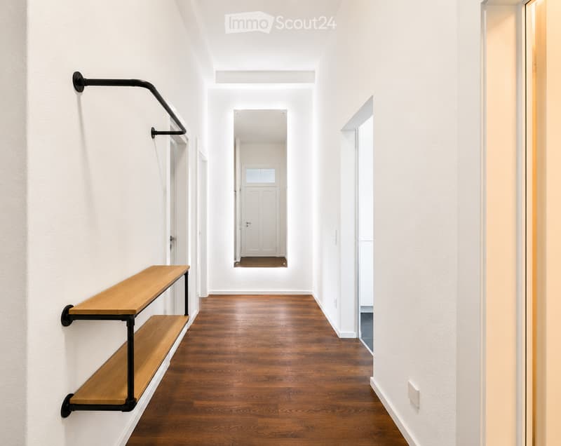 Modern hallway with wooden flooring, white walls, and a black metal shelf unit on the left side.