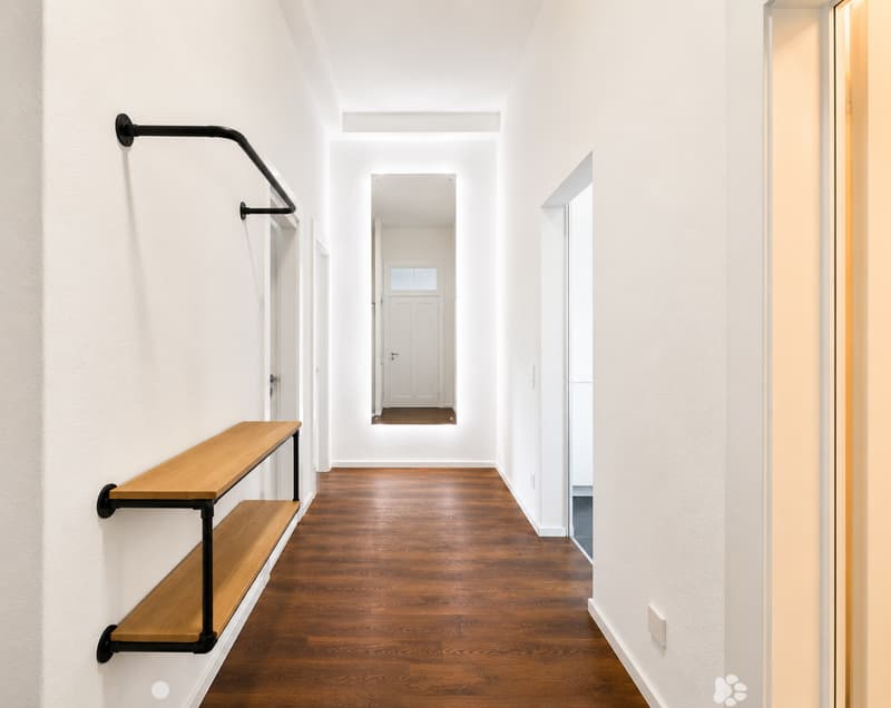 Modern hallway with wooden flooring, white walls, and a black metal shelf unit on the left side.