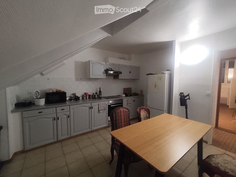 The kitchen features grey cabinets, a refrigerator, an oven, a microwave, a wooden dining table with two chairs, and various kitchen items on the counter.