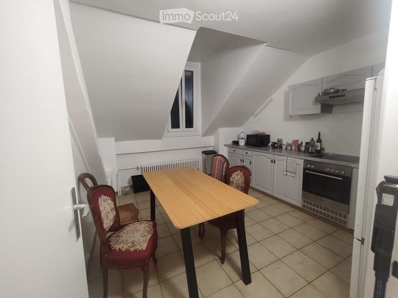 A small, cozy kitchen with a wooden dining table and chairs, white cabinets, and various appliances including an oven and microwave.