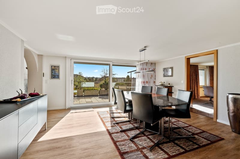 Modern dining room with a sleek black dining table and six chairs, large sliding glass doors leading to a balcony, wooden flooring, and contemporary decor including a vase and picture frame.